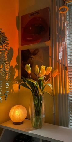 yellow tulips are in a vase next to a lit candle on a table