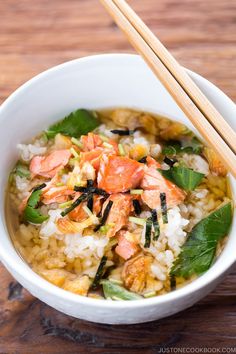 a white bowl filled with rice, meat and veggies next to chopsticks