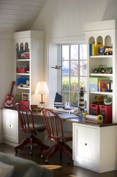 a room with two chairs and a desk in front of a window that has lots of books on it