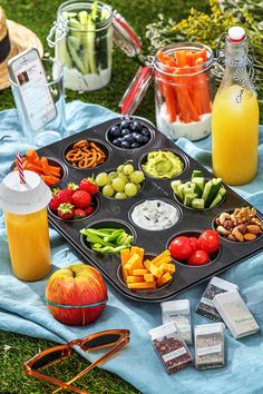 an open book is sitting on a blanket next to a tray of fruit and vegetables