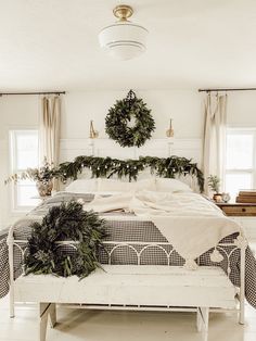 a white bed sitting in a bedroom next to two plants and a wreath on the wall