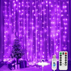 a christmas tree sitting in front of a purple curtain with lights on it and remote controls