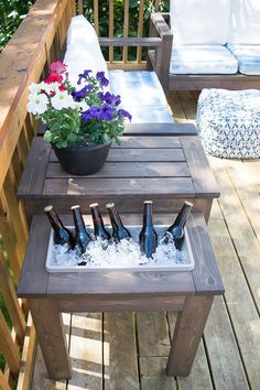 an outdoor table with beer bottles and flowers in it on a wooden deck next to couches