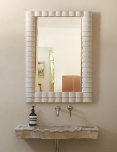 a bathroom sink sitting under a mirror next to a wall mounted faucet with a vase on it