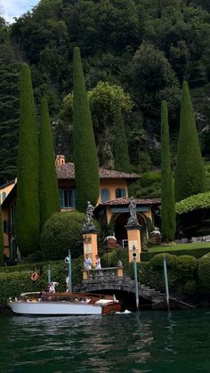 a boat is in the water near some trees and houses on a hill behind it