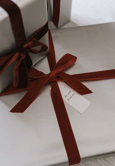 two wrapped gift boxes with red ribbon tied around the top and one white box has a tag on it