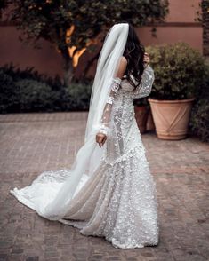 a woman in a wedding dress and veil is standing on a brick walkway with her back to the camera