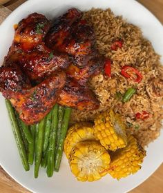 a white plate topped with meat and rice next to corn on the cob, and green beans