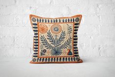 an orange and blue decorative pillow on a white brick wall with a bird in the center