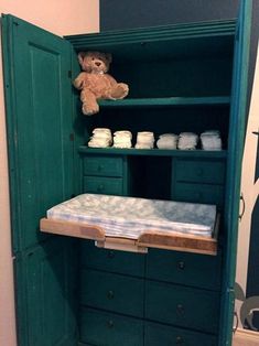 a teddy bear sitting on top of a wooden shelf next to a green cabinet filled with diapers