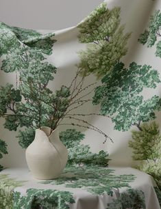 a white vase sitting on top of a table next to a green and white wallpaper