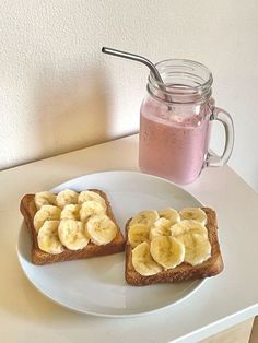 two pieces of toast with banana slices on them and a pink smoothie in the background