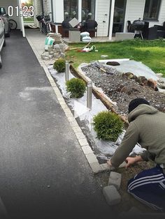 a man kneeling down in front of a house next to a yard filled with potted plants