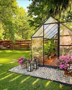 a small greenhouse in the middle of a yard with potted plants and flowers inside