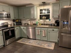 a kitchen with green cabinets and stainless steel appliances, along with an area rug on the floor