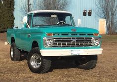 an old green truck parked in front of a blue building