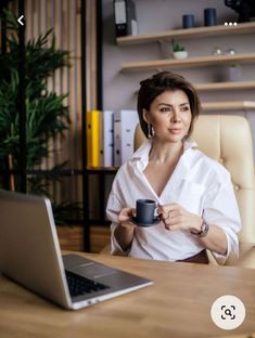 a woman sitting at a desk with a laptop and coffee cup in front of her