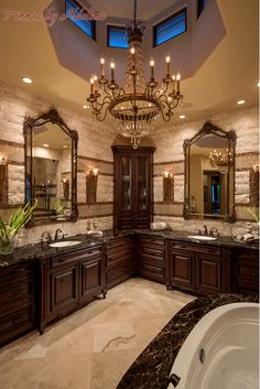 a fancy bathroom with chandelier and marble counter tops, two sinks, large bathtub