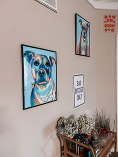 three framed pictures hang on the wall above a dining room table with flowers in front of it