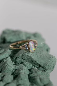 an opal and diamond ring sitting on some rocks