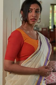 a woman in an orange and white sari is posing for the camera with her hand on her hip