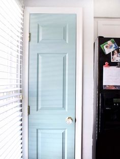 a blue door in the corner of a room next to a black refrigerator with magnets on it