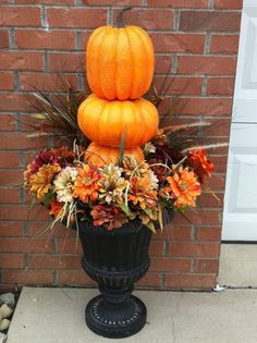 a tall black vase filled with lots of flowers and pumpkins on top of it