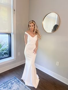 a woman standing in front of a window wearing a white dress and holding her hands on her hips