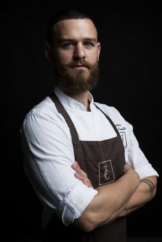 a bearded man with his arms crossed wearing an apron