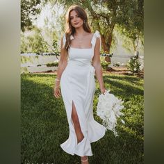 a woman in a white dress holding a bouquet and posing for a photo on the grass