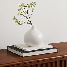 a white vase sitting on top of a wooden table next to a stack of books