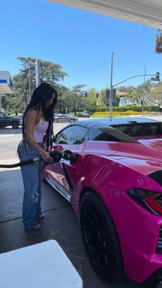 a woman pumping gas into her pink sports car