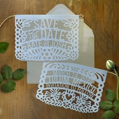 two laser cut save the date cards on top of a wooden table with green leaves