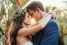 a bride and groom embracing each other in front of palm trees with the sun behind them