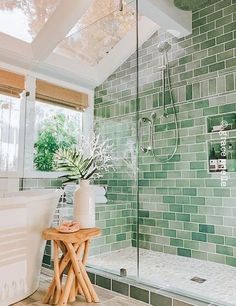 a green tiled bathroom with a wooden stool and glass shower door that opens up to the outside