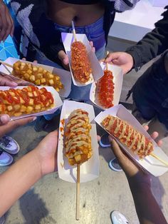 several people holding up trays of food with skewers on them and toppings