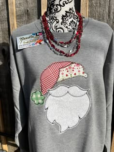 a gray sweater with a santa hat on it and a red beaded necklace hanging from the neck