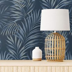 a lamp on a table next to a palm leaf wallpaper and a white vase