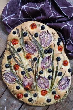 a pizza topped with onions and blueberries on top of a wooden table