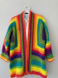 a multicolored crocheted cardigan hanging on a white wall next to a hanger