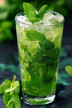 a glass filled with ice and mint on top of a table next to green leaves