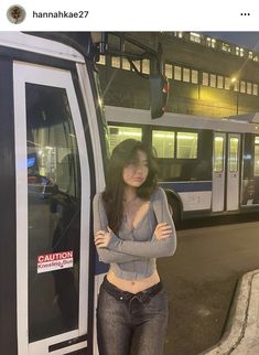 a woman standing next to a bus in front of a building with her arms crossed