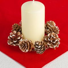 a white candle sitting on top of a red place mat with pine cones around it