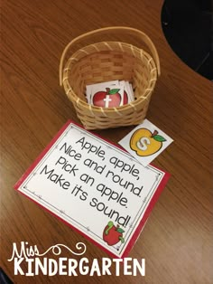 a basket with some cards and an apple in it sitting on a table next to a sign