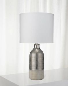 a lamp that is on top of a table next to a white wall and window