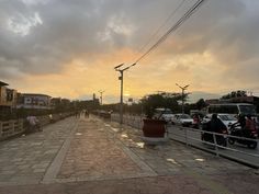 the sun is setting on an overcast day with people walking and riding bikes in the street