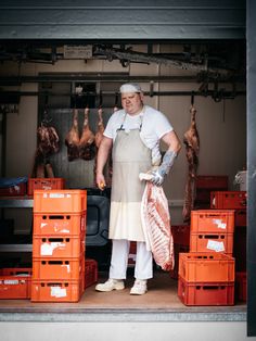 a man in an apron holding some meat and standing next to crates with dead chickens