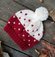 a red and white knitted hat with hearts on it sitting on a wooden surface