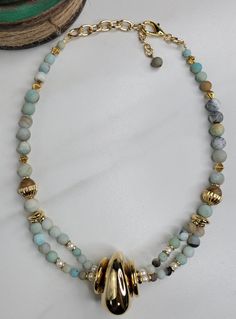 Our River necklace is handmade with amazonite beads which are known for their soothing properties. A few natural freshwater pearls are sprinkled among the blue amazonite beads. The River necklace features a vintage Italian gold plated bead that is like a stone shaped by moving water, smooth and inviting. This gorgeous statement piece is handmade in the United States. A coordinating bracelet and set of earrings is available. Features: - Italian Vintage Elements from 1980s - Gold Plated Cable Chai Elegant Amazonite Beaded Necklaces With Natural Stones, Gift Amazonite Beaded Necklace With Polished Beads, Elegant Adjustable Amazonite Beaded Necklaces, Elegant Amazonite Beaded Necklace With Natural Stones, Adjustable Amazonite Beaded Necklaces, Elegant Handmade Amazonite Beaded Necklace, Adjustable Amazonite Necklace With Polished Beads, Handmade Amazonite Round Beads Necklaces, Artisan Amazonite Round Bead Necklace