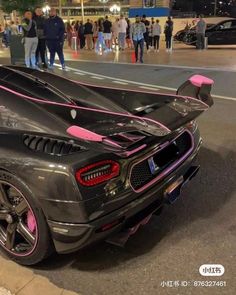 a black sports car with pink stripes parked on the street